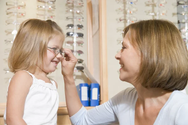 La mujer probando las gafas a la muchacha joven a los optometristas sonriendo — Foto de Stock