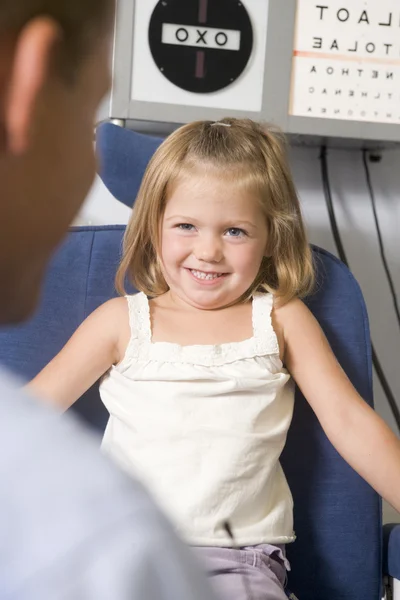 Optometrista en sala de examen con chica joven en silla sonriendo —  Fotos de Stock