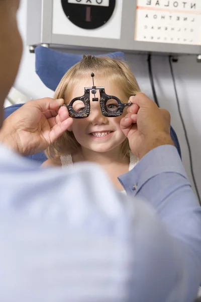 Optiker i examen rummet med ung flicka i stol leende — Stockfoto
