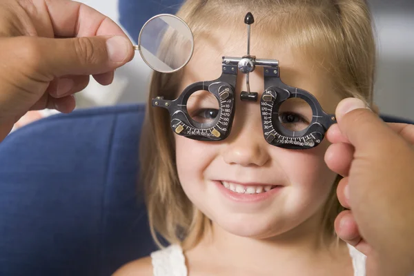 Optometrista en sala de examen con chica joven en silla sonriendo — Foto de Stock