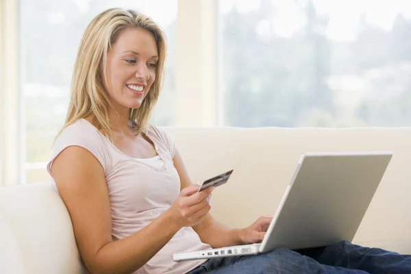 Женщина в гостиной с ноутбуком и с улыбкой на кредитке — стоковое фото