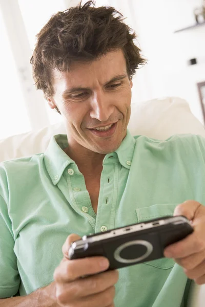 Мужчина в гостиной играет в ручную видеоигру улыбаясь — стоковое фото
