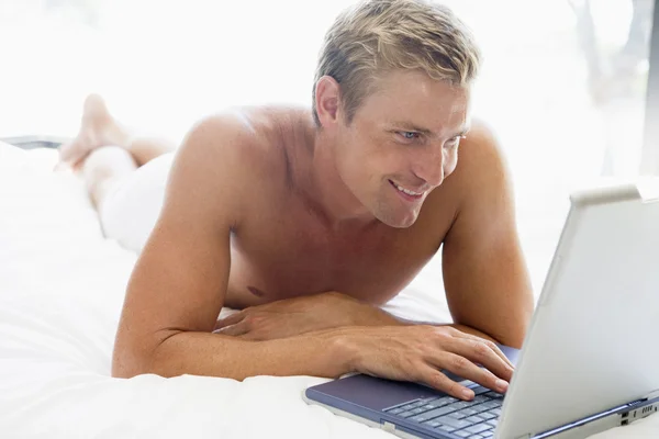 Muž leží v posteli s úsměvem a notebook — Stock fotografie