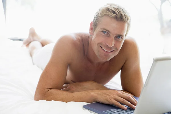 ラップトップを笑顔でベッドに横たわっている男 — ストック写真