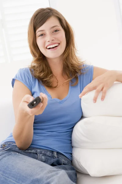 Vrouw in woonkamer met afstandsbediening lachende — Stockfoto