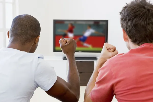 Two men in living room watching television and cheering — Stock Photo, Image