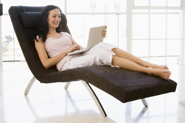 Жінка сидить у кріслі, використовуючи ноутбук посміхаючись — стокове фото