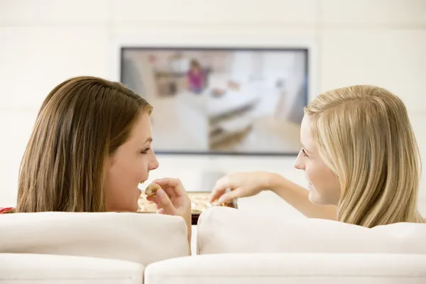 Två kvinnor i vardagsrummet framför TV äta choklad s — ストック写真