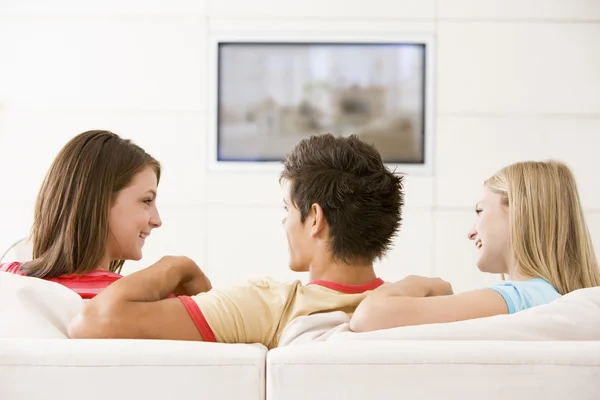 Три друга в гостиной смотрят телевизор улыбаясь — стоковое фото