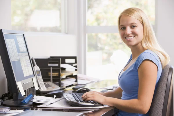 Женщина в домашнем офисе с помощью компьютера и улыбаясь — стоковое фото