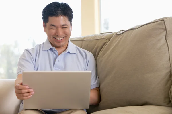 Mann im Wohnzimmer benutzt Laptop und lächelt — Stockfoto