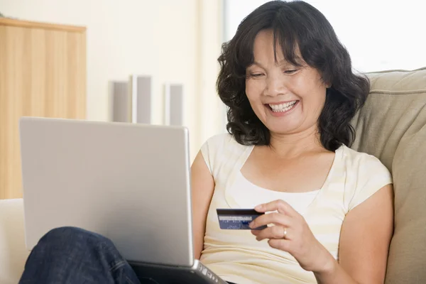 在客厅里使用的便携式计算机持有信用卡和微笑的女人 — 图库照片