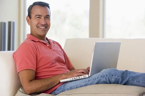 在使用笔记本电脑微笑的客厅里的男人 — 图库照片