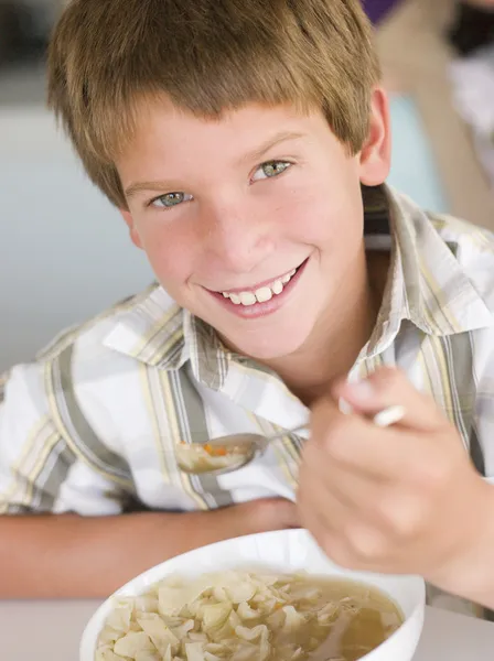 Jonge jongen in keuken eten van soep en glimlachen — Stockfoto
