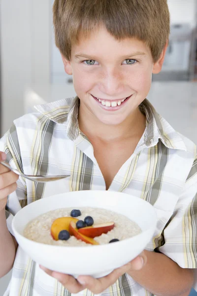 Młody chłopak w kuchni jeść płatki owsiane z owocami uśmiechający się — Zdjęcie stockowe