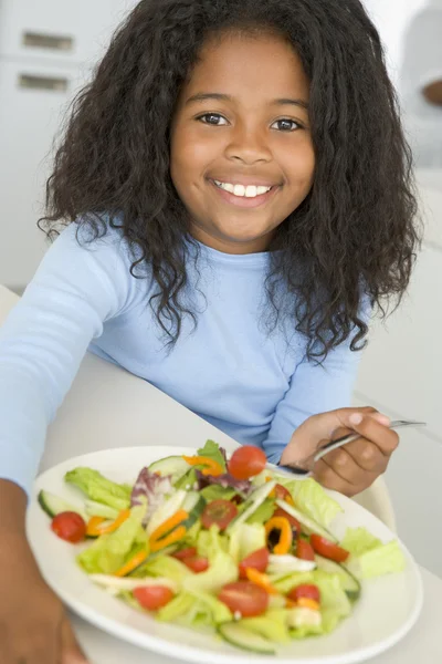 Νεαρή κοπέλα στην κουζίνα που τρώει σαλάτα χαμογελώντας — Φωτογραφία Αρχείου