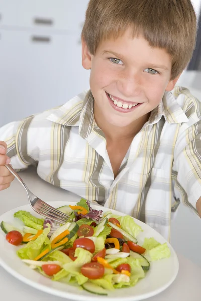 在厨房里吃沙拉微笑的小男孩 — 图库照片