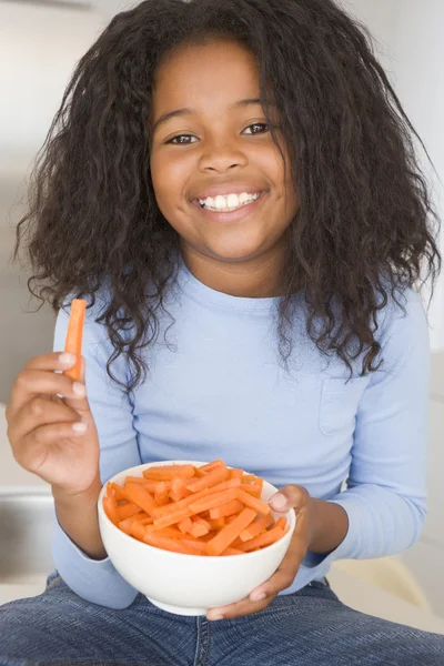 Νεαρή κοπέλα στην κουζίνα, τρώγοντας καρότο μπαστούνια χαμογελώντας — Φωτογραφία Αρχείου