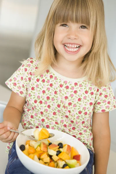 Jong meisje in keuken eten kom fruit glimlachen — Stockfoto
