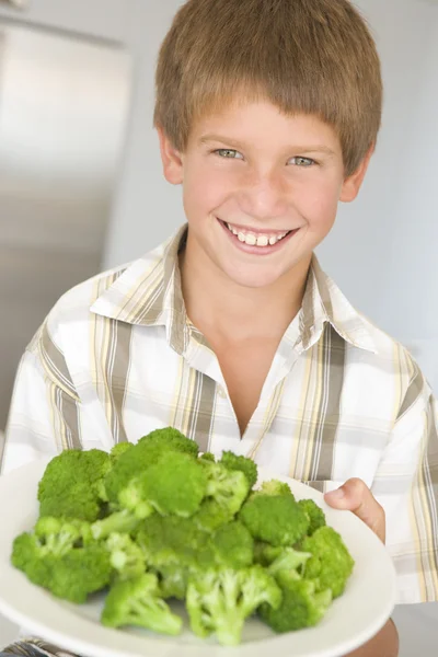 Ung pojke i köket äter broccoli leende — Stockfoto