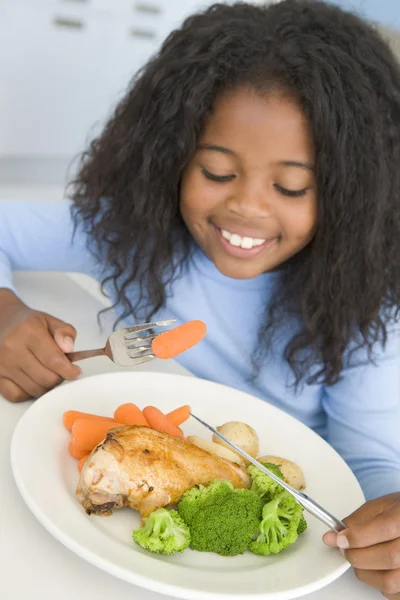 Νεαρή κοπέλα στην κουζίνα που τρώει το κοτόπουλο και τα λαχανικά που είναι χαμογελώντας — Φωτογραφία Αρχείου