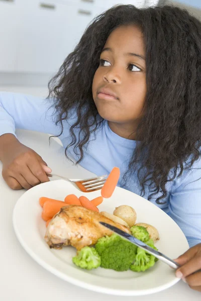 Молодая девушка на кухне ест курицу и овощи — стоковое фото