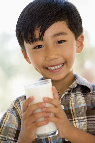 Мальчик в помещении пьет молоко улыбаясь — стоковое фото