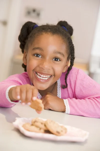 Молодая девушка на кухне ест печенье улыбаясь — стоковое фото