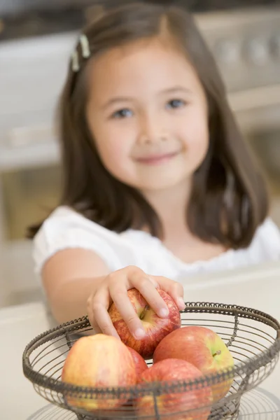 Молодая девушка на кухне снимает яблоко со стола улыбаясь — стоковое фото