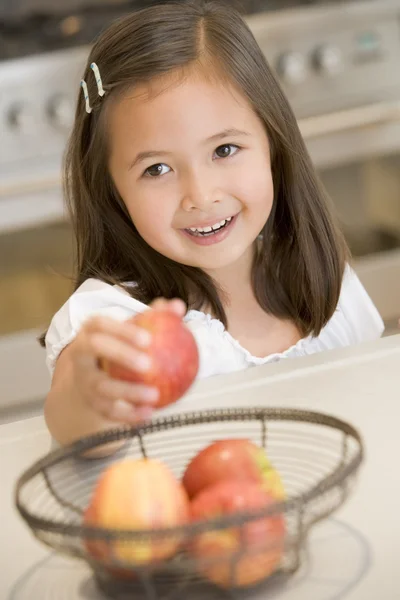 Young girl in kitchen getting apple off counter smiling — Stock Photo, Image