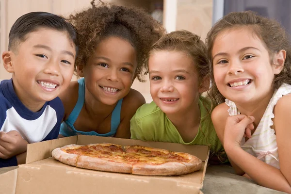 Четверо маленьких детей в помещении едят пиццу улыбаясь — стоковое фото