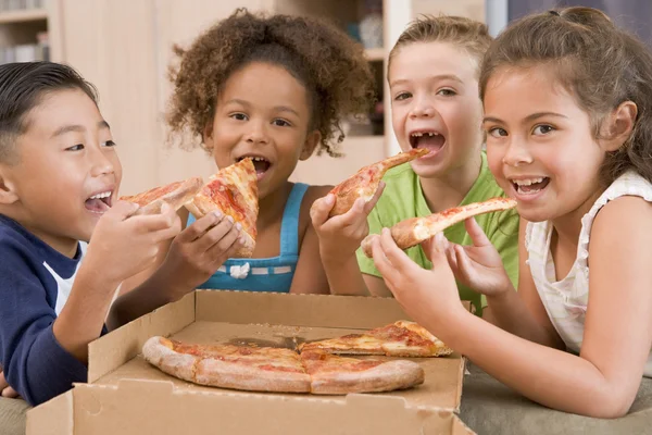 Vier jonge kinderen binnenshuis eten pizza glimlachen — Stockfoto