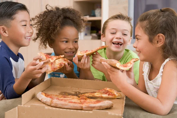 四个年轻孩子在室内吃披萨微笑 — 图库照片