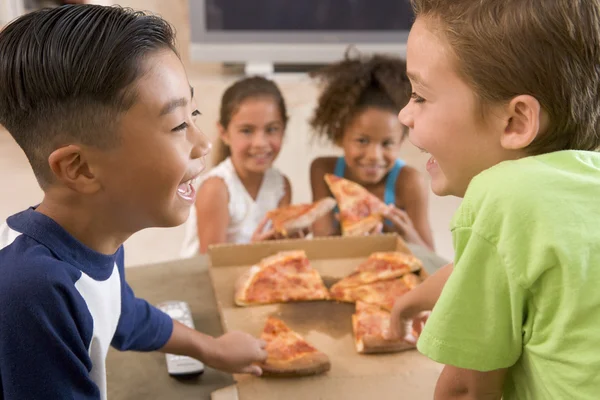 Vier jonge kinderen binnenshuis eten pizza glimlachen — Stockfoto