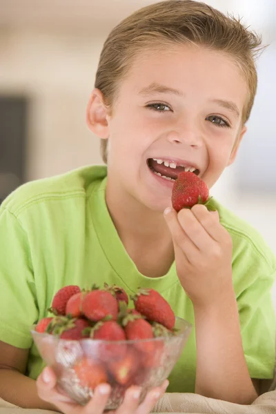 リビング ルームの笑顔でイチゴを食べる若い男の子 — ストック写真