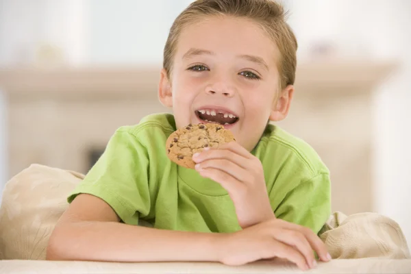 Мальчик ест печенье в гостиной улыбаясь — стоковое фото