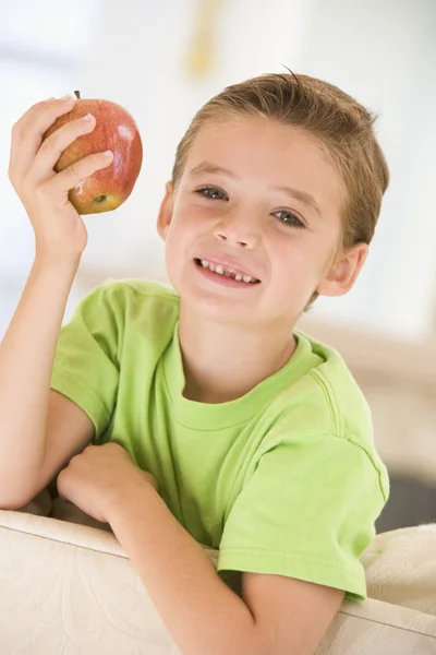 Junge isst lächelnd Apfel im Wohnzimmer — Stockfoto