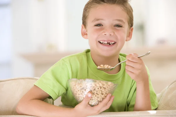 Mladý chlapec jíst obiloviny v obýváku s úsměvem — Stock fotografie