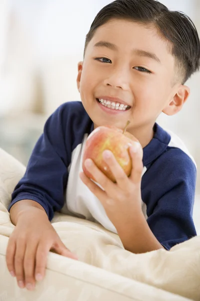Молодий хлопчик їсть яблуко у вітальні посміхається — стокове фото