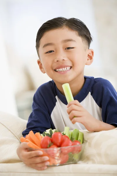 Kleiner Junge isst Schüssel mit Gemüse im Wohnzimmer lächelnd — Stockfoto