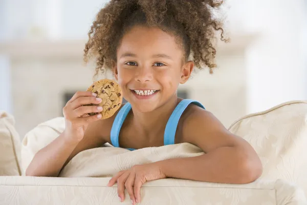 リビング ルームの笑顔でクッキーを食べる若い女の子 — ストック写真