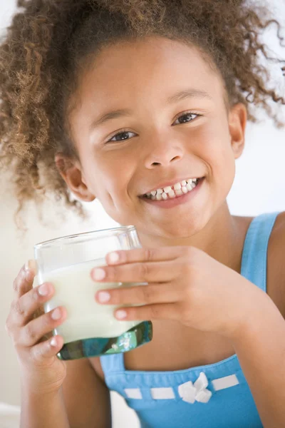 Молодая девушка в помещении пьет молоко улыбаясь — стоковое фото