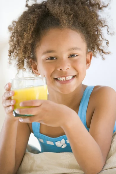年轻女孩喝橙汁在客厅里微笑 — 图库照片
