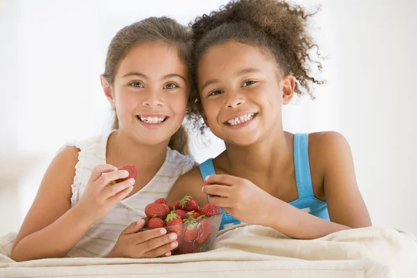 Zwei junge Mädchen, die im Wohnzimmer lächelnd Erdbeeren essen — Stockfoto