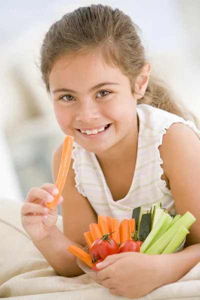 年轻的女孩吃碗蔬菜的客厅里微笑 — 图库照片