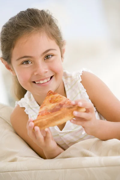 年轻的女孩吃披萨片在客厅里微笑 — 图库照片