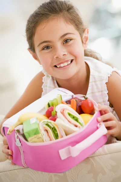 Chica joven sosteniendo el almuerzo lleno en la sala de estar sonriendo —  Fotos de Stock
