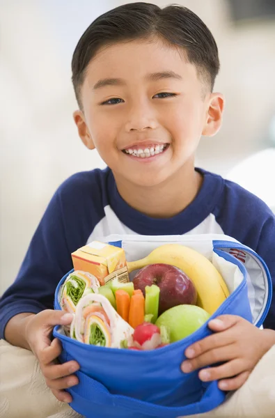 Jonge jongen binnenshuis met Lunchpakket glimlachen — Stockfoto
