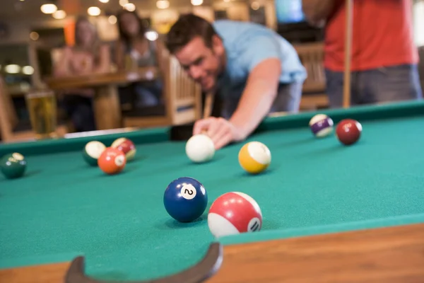 Young man playing pool in a bar (focus on pool table) Royalty Free Stock Photos