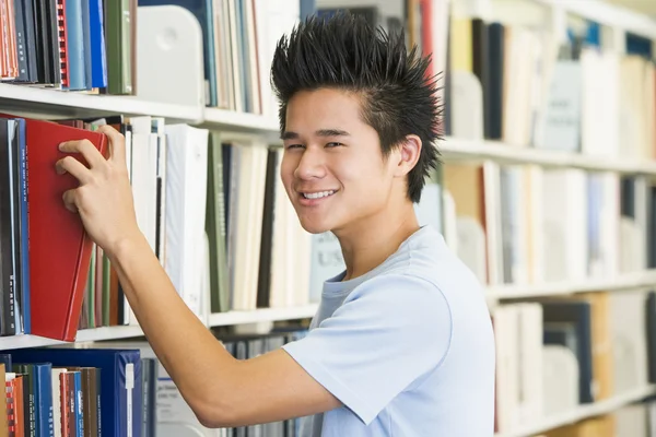 Estudiante universitario seleccionando libro del estante de la biblioteca Fotos De Stock Sin Royalties Gratis